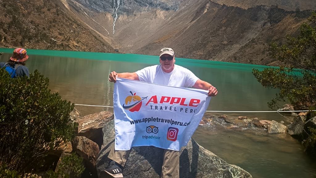 A smiling male tourist with Apple Travel Peru's flag at Humantay Lake